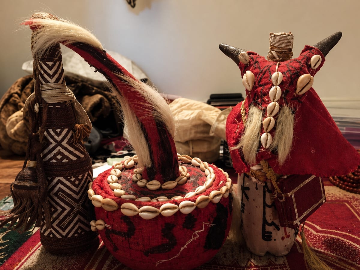 Statuettes de protection en cauris, cornes et étoffe rouge posées sur un tapis